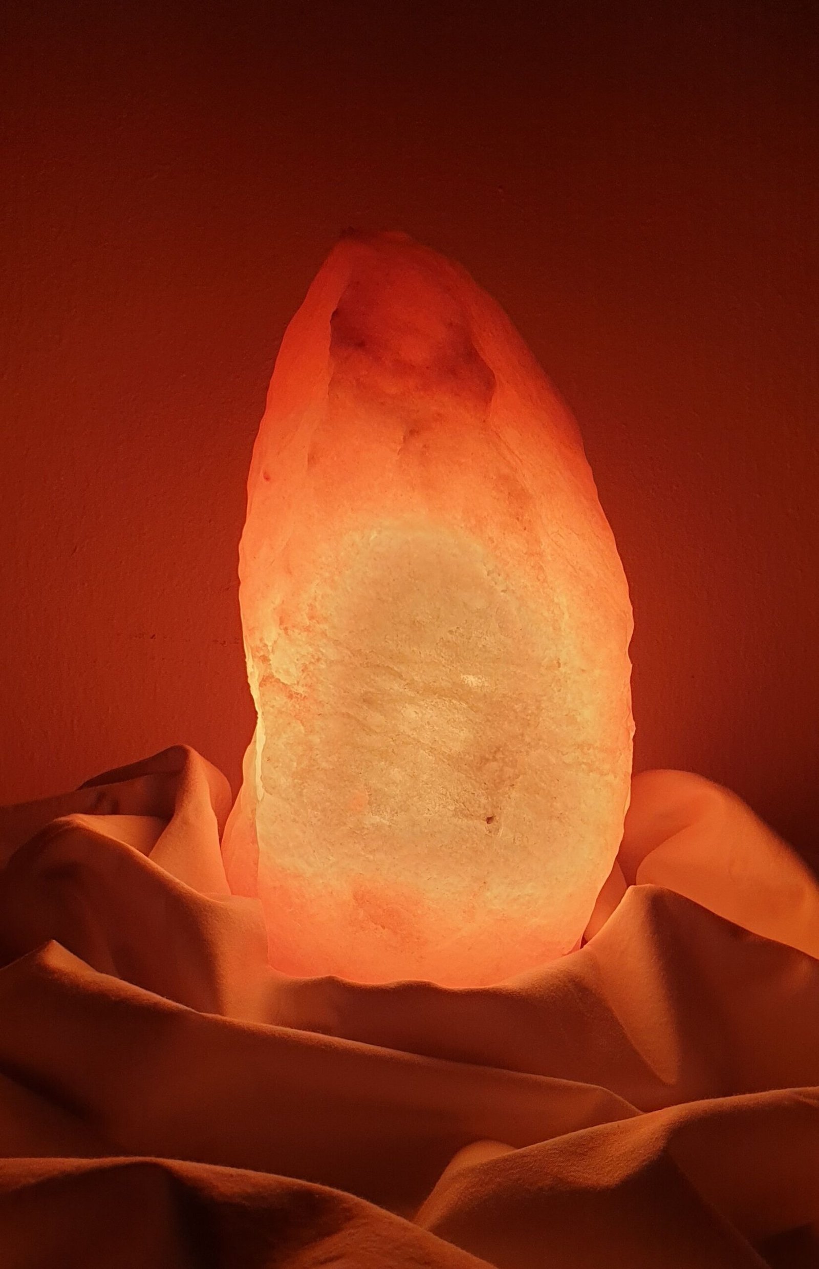 Glowing Himalayan salt lamp placed on draped fabric, creating a warm ambiance.
